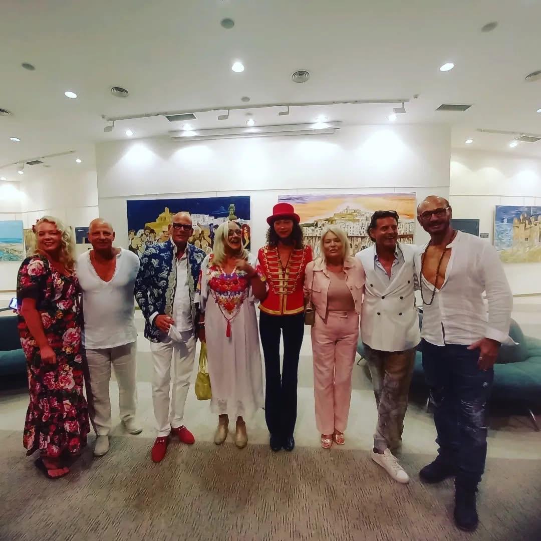 Nine guests posed together at an opening, canvases hung behind them