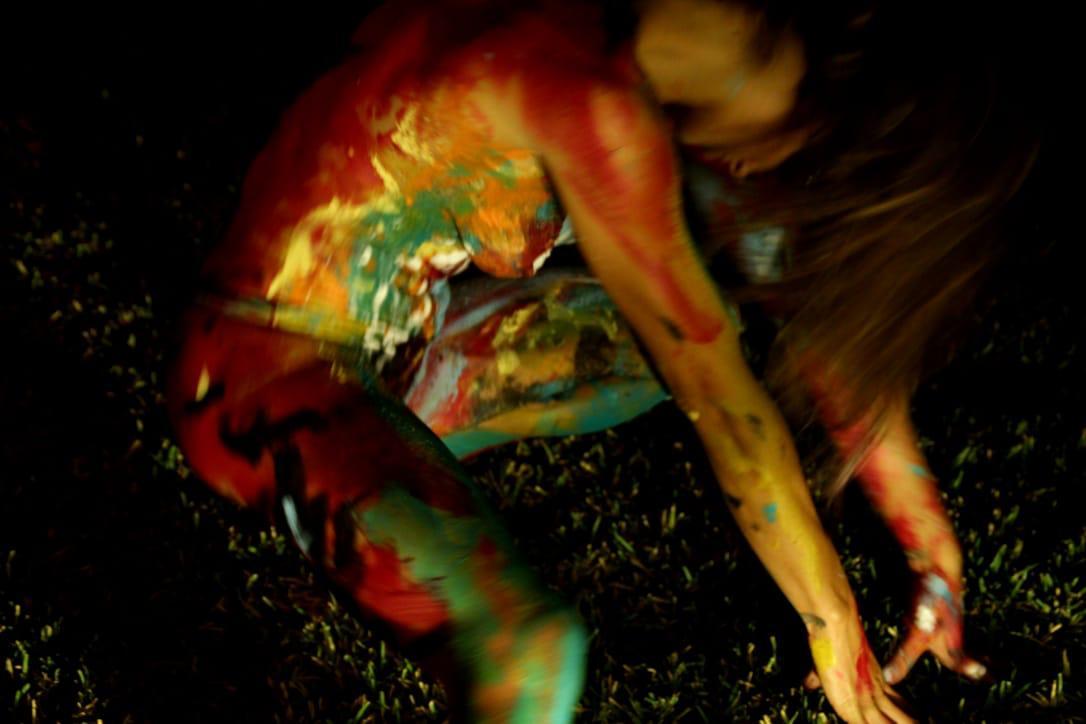 A body-painted figure moving through the dark, caught mid-motion