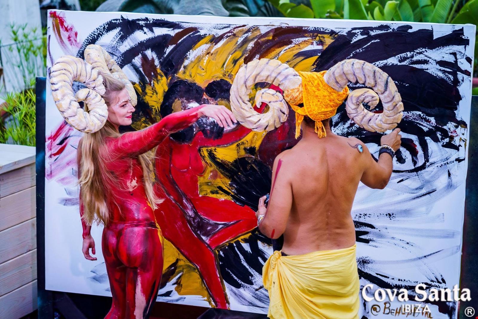 Painting with two body-painted performers in horned headdresses at Cova Santa