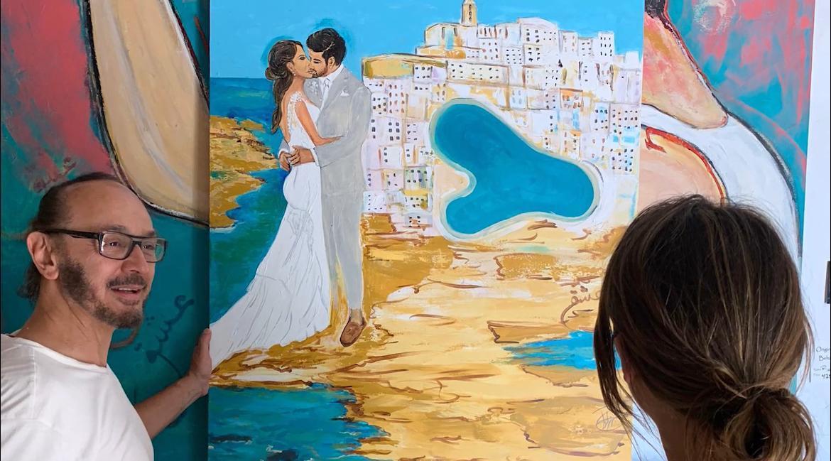 A guest looking at a wedding commission — the couple painted above a turquoise bay