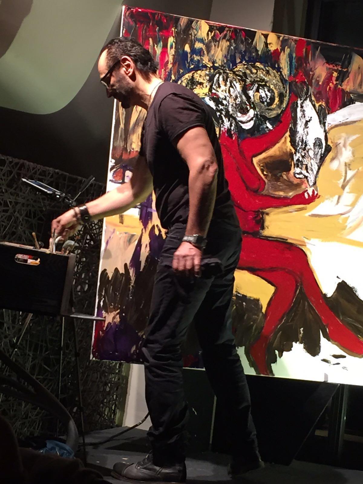 Behzad painting live at an event, working into a red and black canvas
